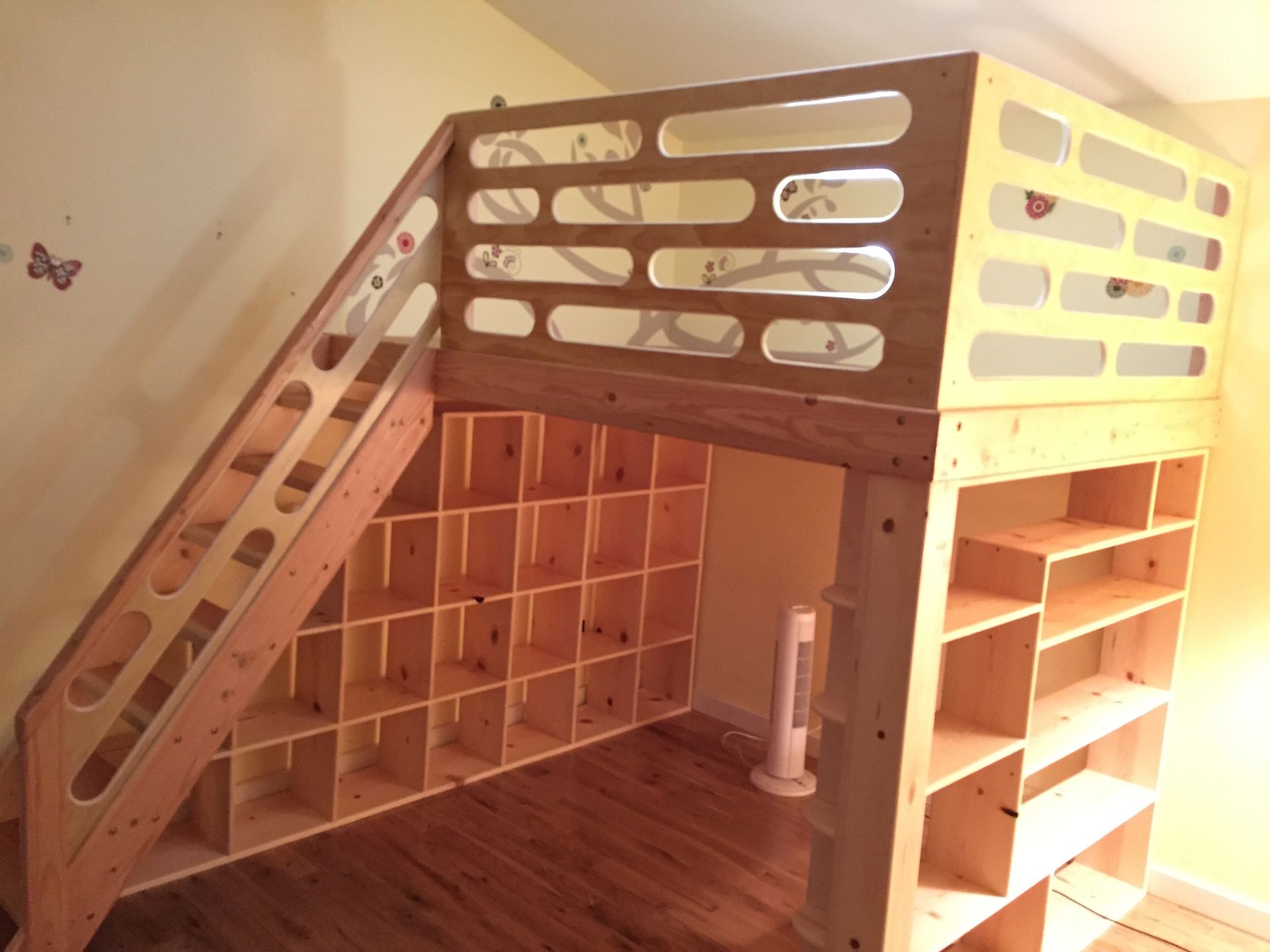 A wooden loft bed with a built-in staircase featuring open cubby storage underneath and shelving on the side.