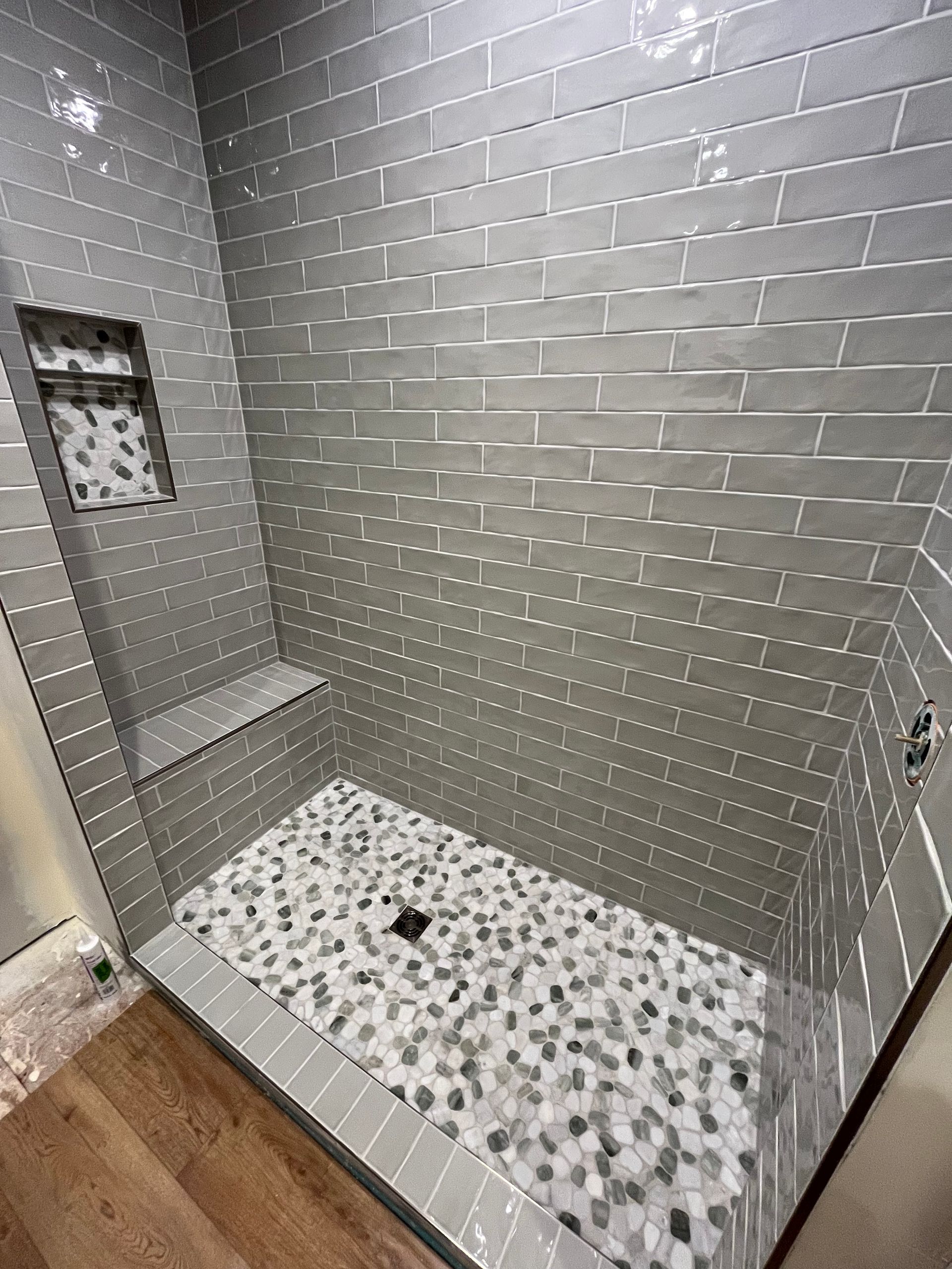 A walk-in shower with gray subway wall tiles, a built-in bench, and a textured pebble floor.