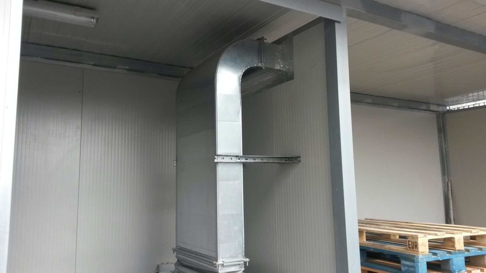 Un magazzino con pallet sul pavimento e un tubo di metallo che esce dal soffitto.