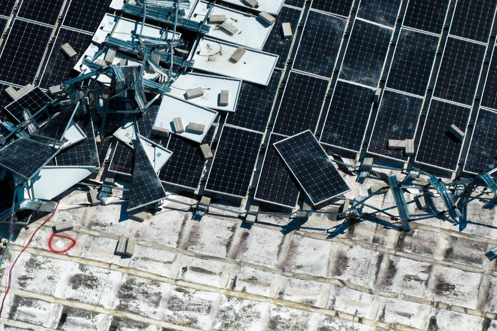 Aerial perspective of shattered solar panels scattered across the rooftop of an industrial building, depicting the aftermath of destruction.