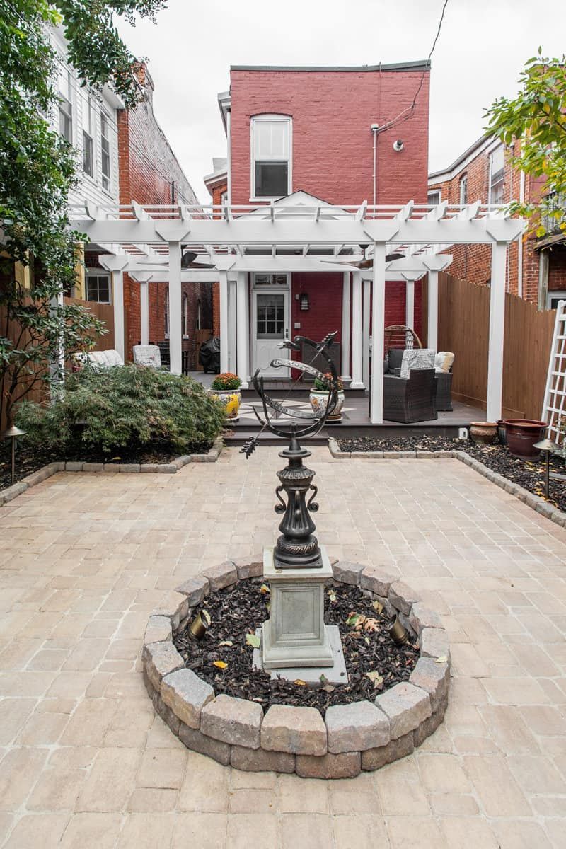 Backyard patio with a brick pathway, pergola, and decorative fountain.