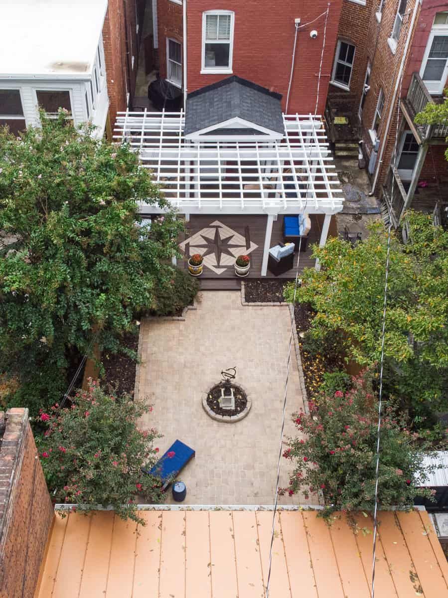 Overhead view of a brick courtyard with a small fountain, surrounded by trees and a pergola-covered patio.