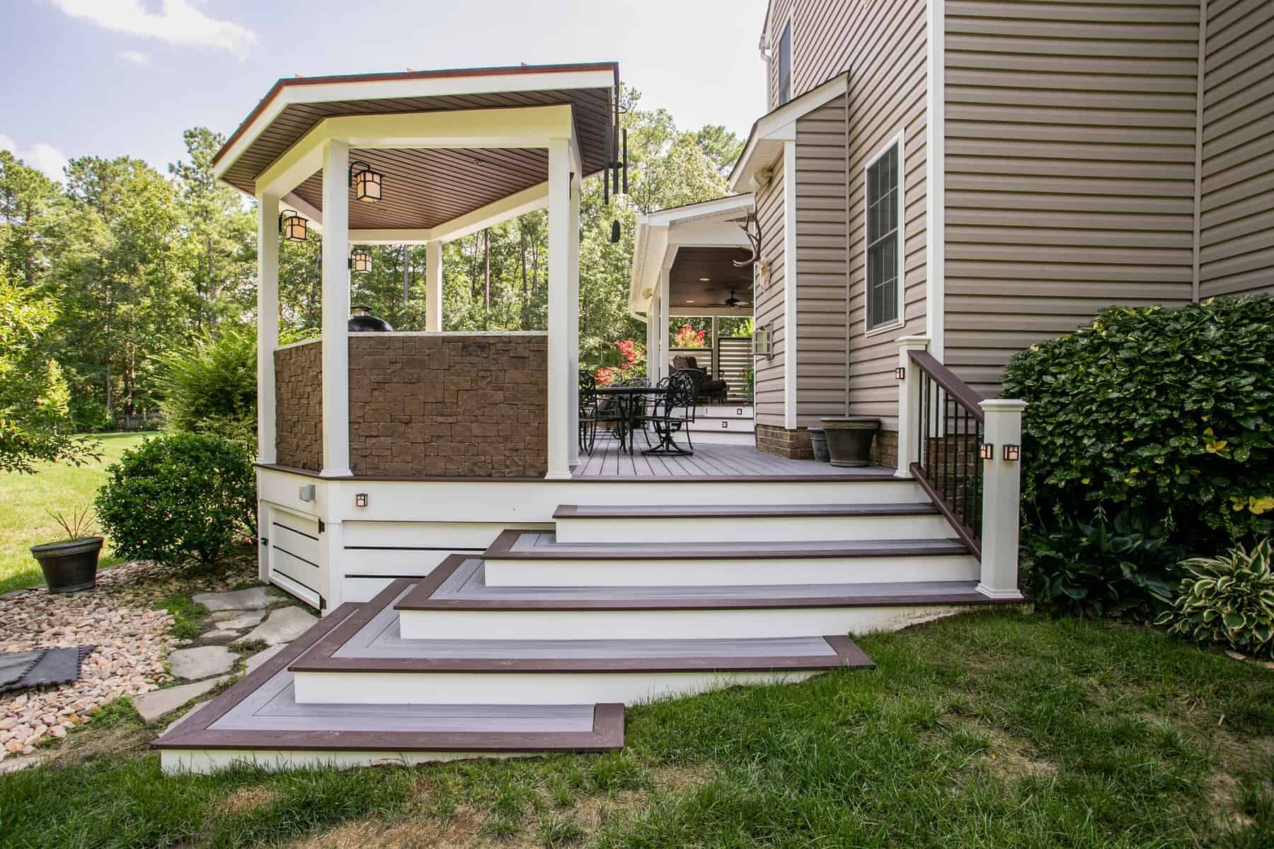 Wooden deck with stairs leading to a gazebo; house with light siding and green lawn.