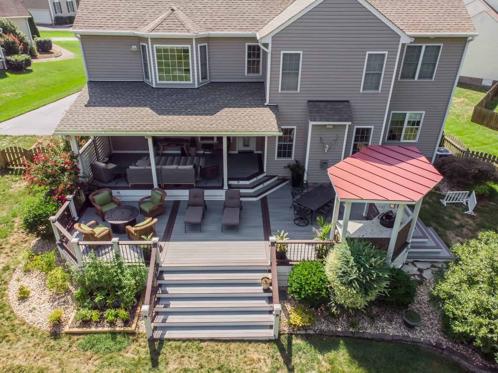 Backyard deck with gray siding house, gazebo, and seating areas.