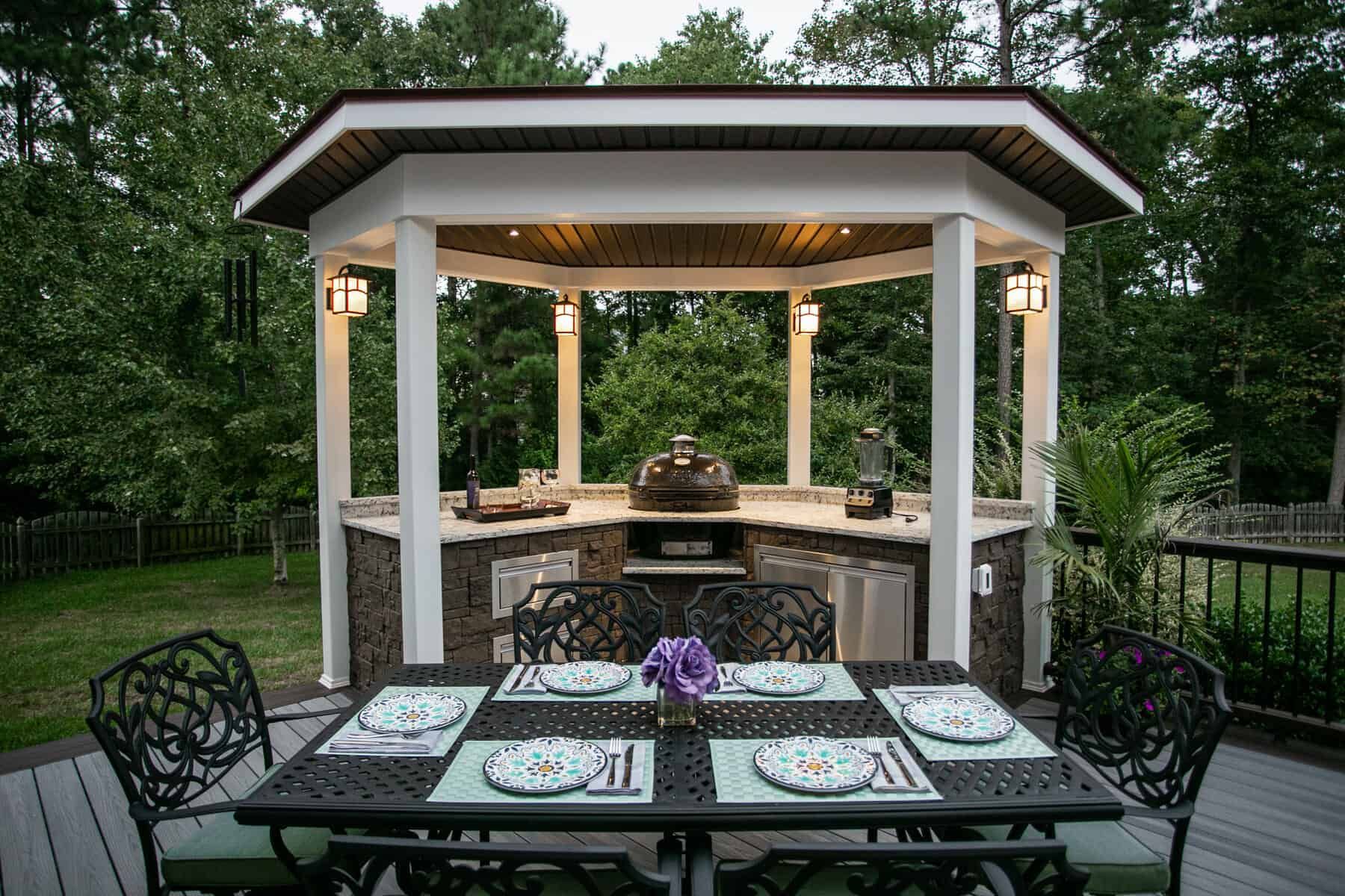 Outdoor kitchen with a grill, countertops, and dining table set for a meal.