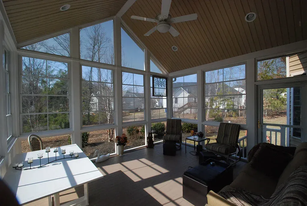 Sunroom with large windows, vaulted ceiling, and outdoor furniture. Sunlight streams in.