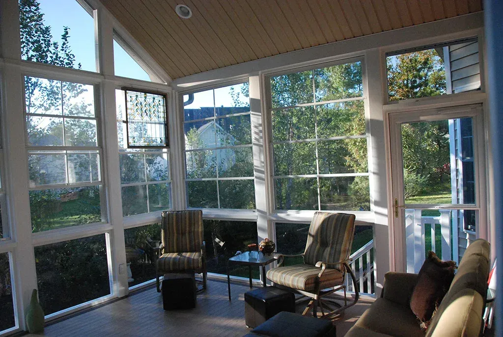 Sunroom with large windows and chairs, overlooking trees.