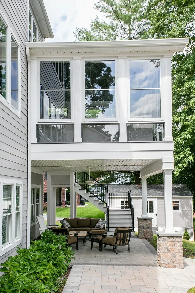 Covered porch with seating area and glass-walled upper level overlooking a yard.