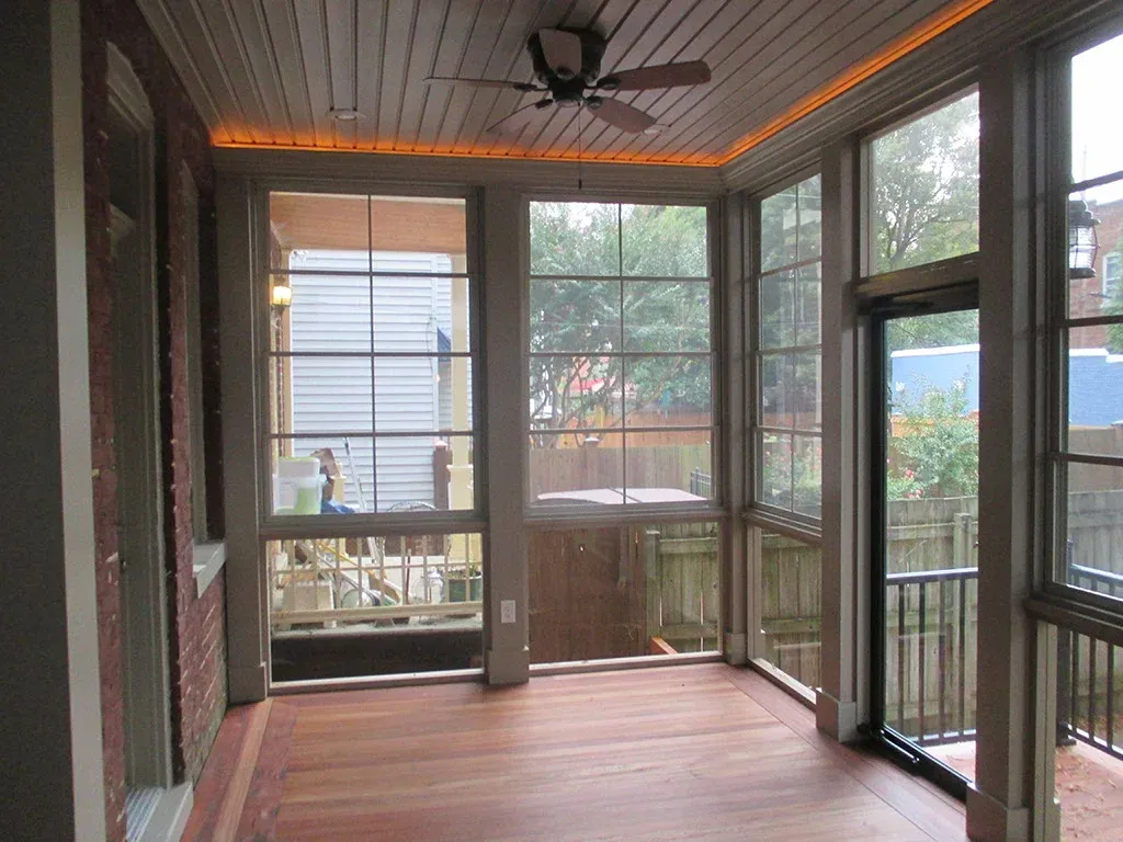 Enclosed porch with wood floors, large windows, ceiling fan, and brick wall.