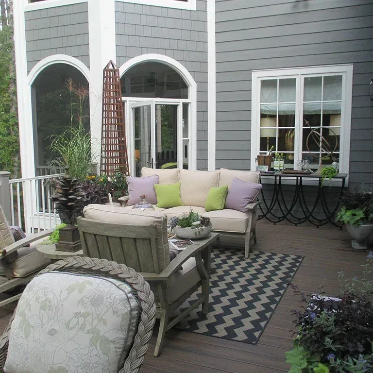 Patio with seating, outdoor rug, and plants against gray house.