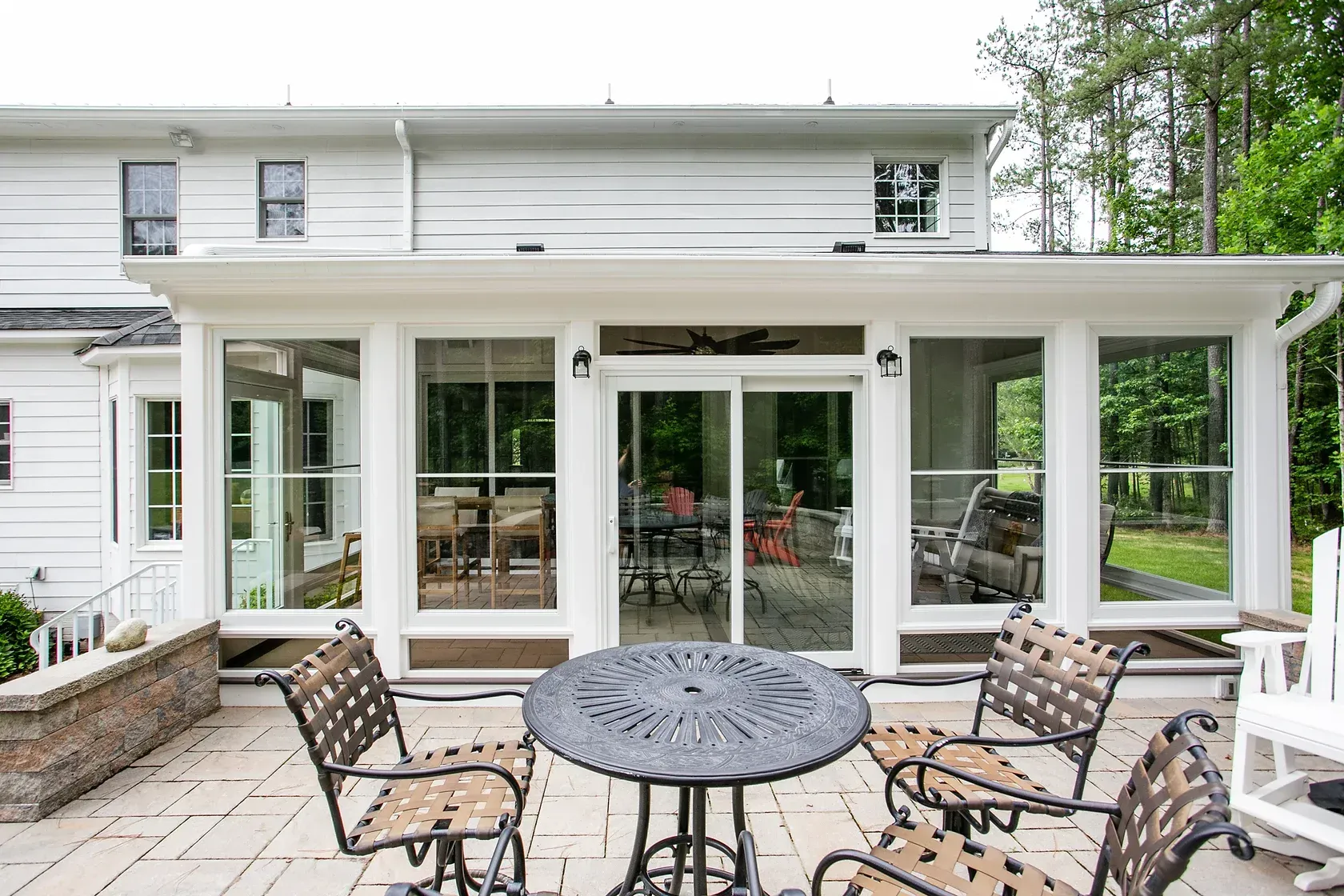 White sunroom addition with sliding glass doors, attached to a house. Patio furniture sits in front.