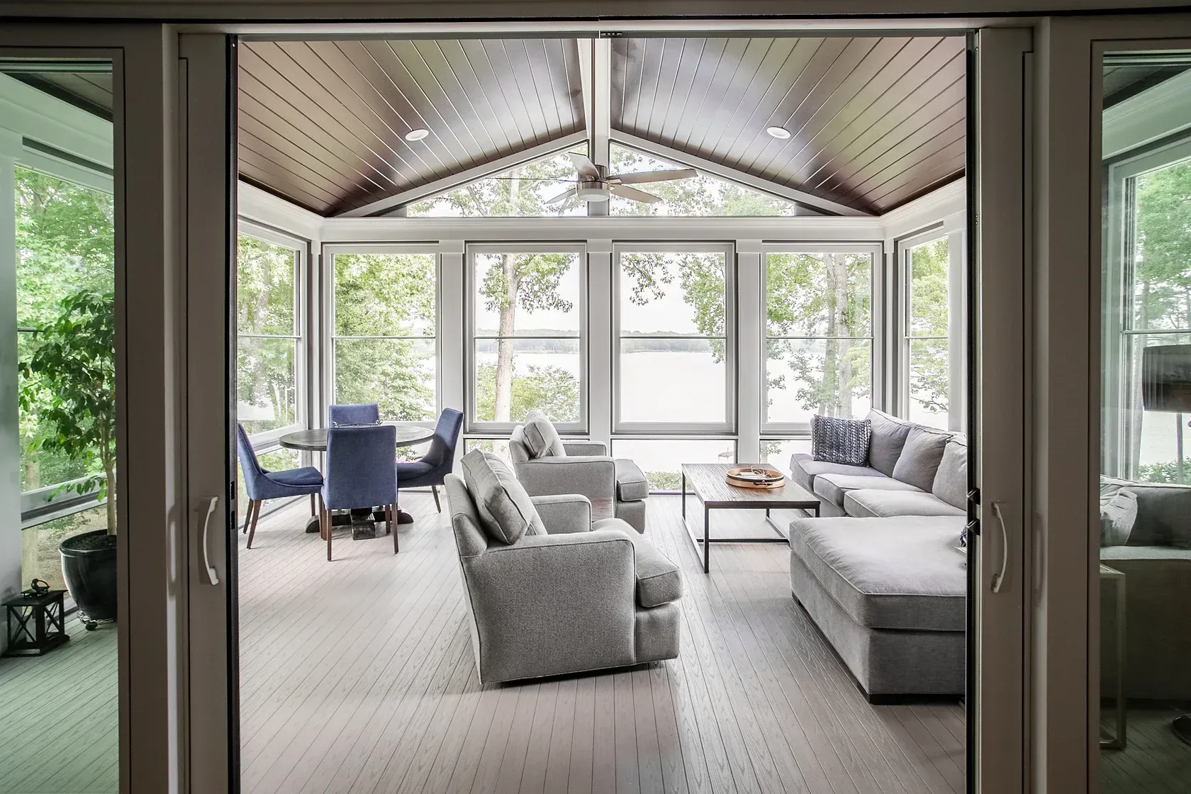 Sunroom with seating, dining table, and large windows overlooking a lake.