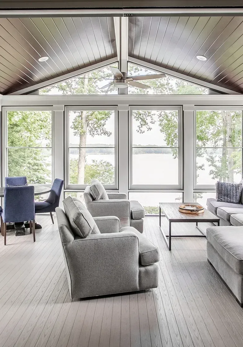 Living room with lake view, gray furniture, wood ceiling, large windows.