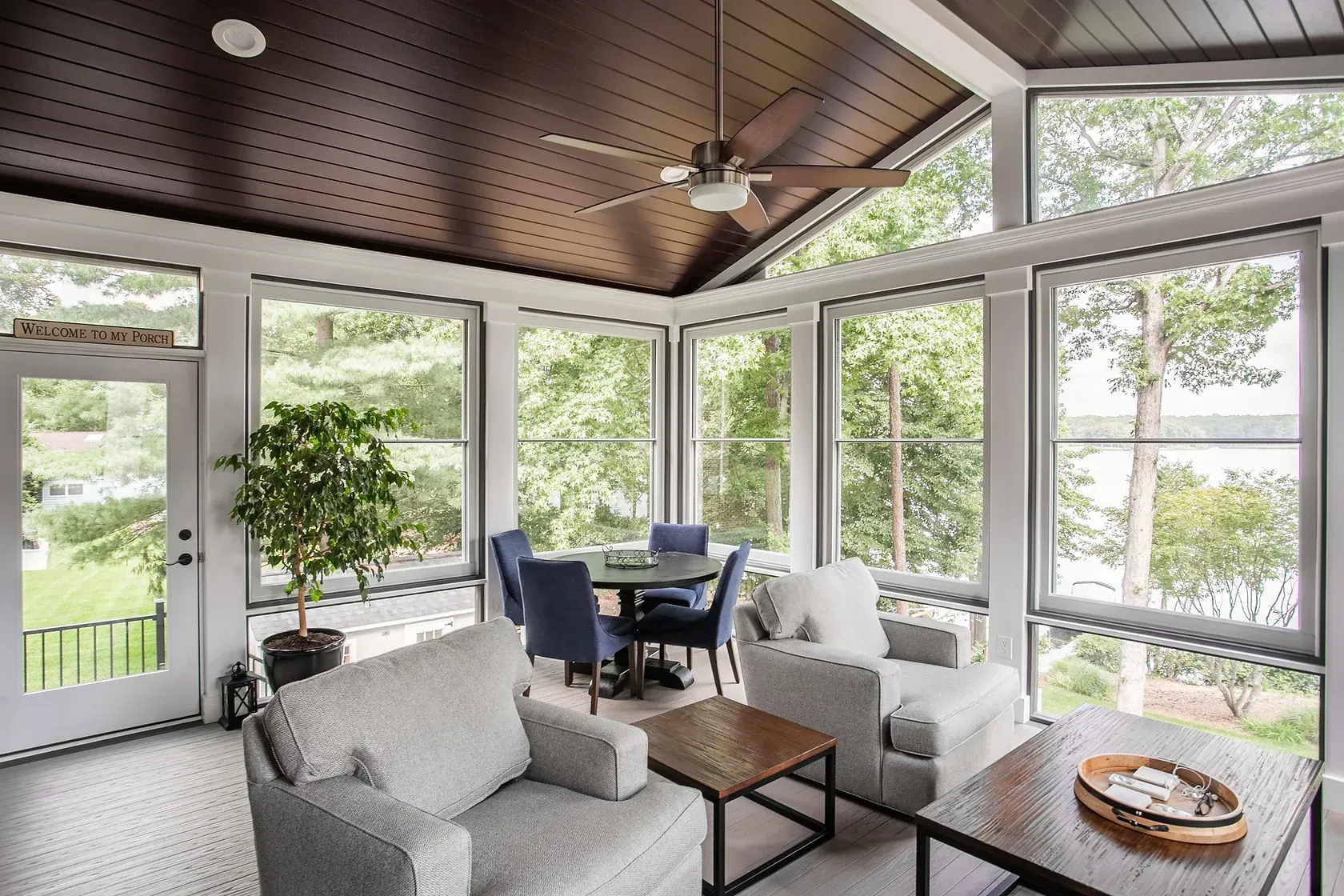 Sunroom with windows overlooking a lake, furnished with seating and a dining table.