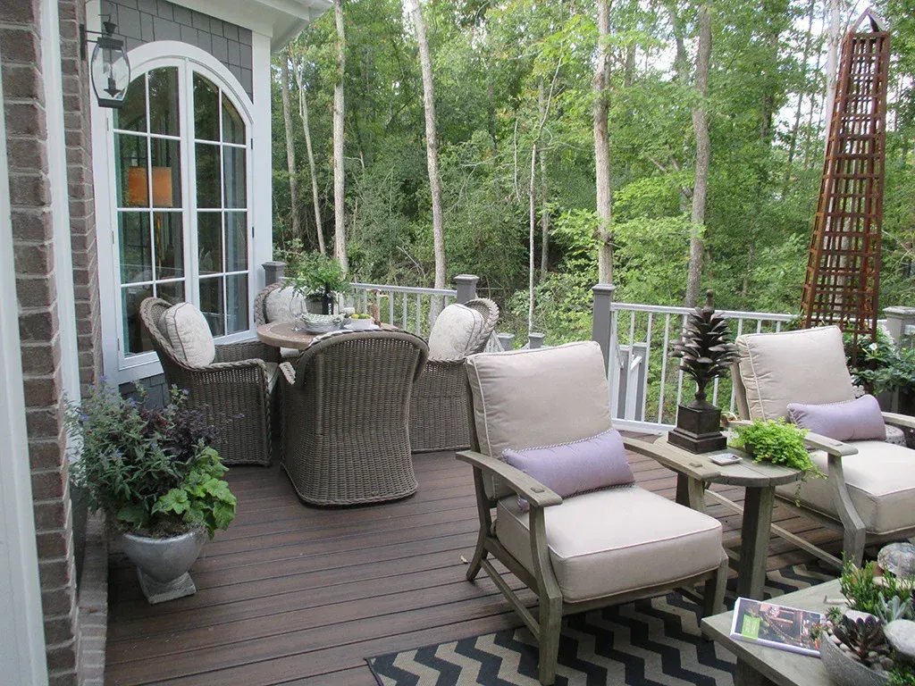 Outdoor deck with wicker furniture, potted plants, and wooded background.
