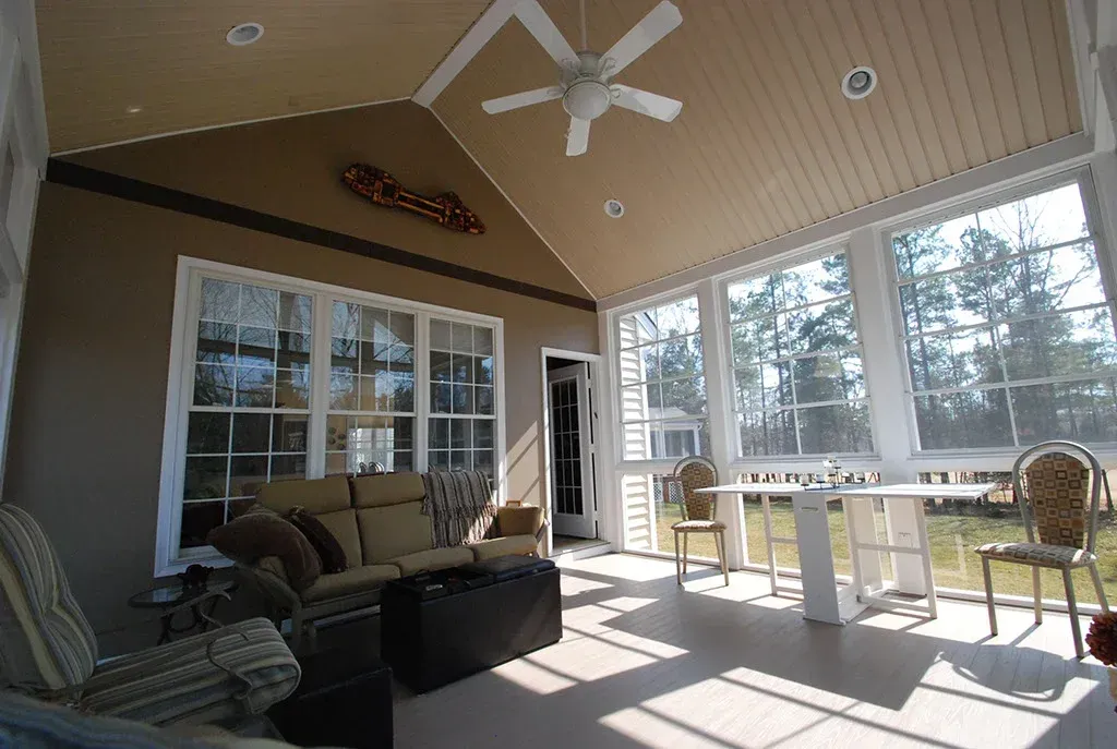 Sunroom with a sofa, chairs, table, and windows overlooking trees.