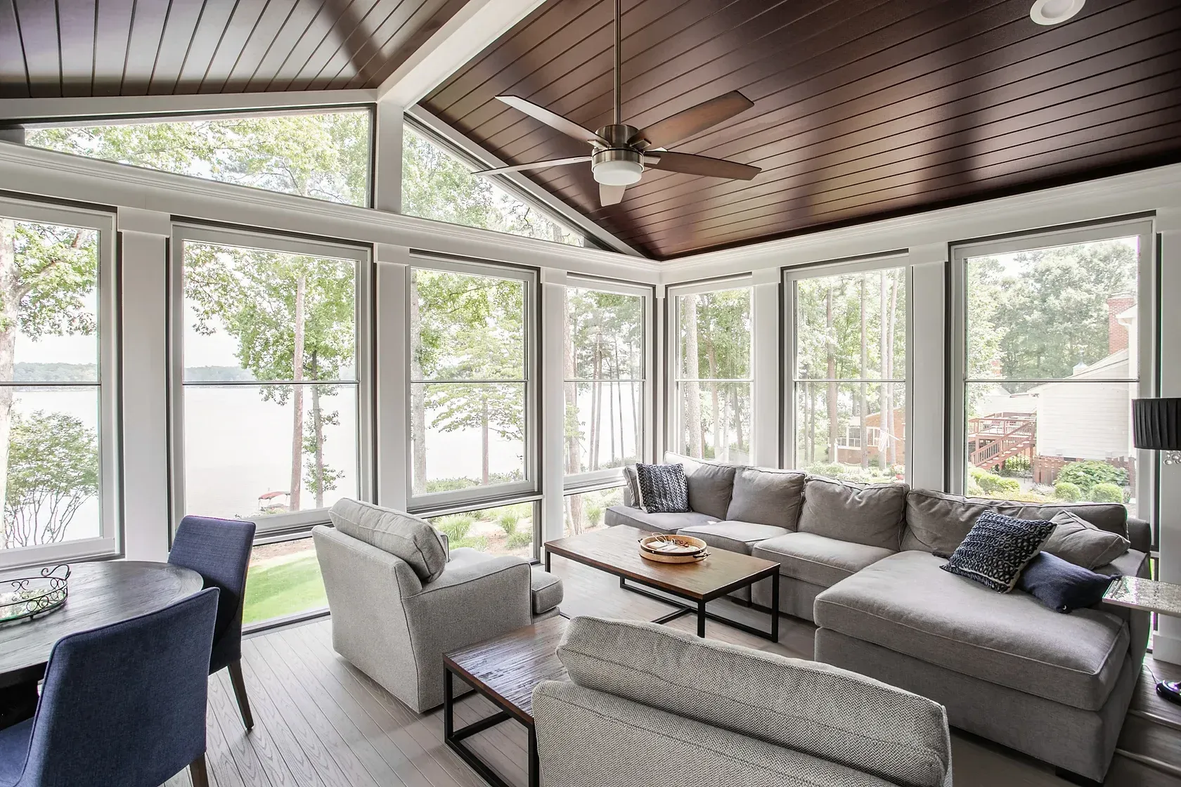 Sunroom with large windows, lake view, seating area with sofa, chairs, and dark ceiling fan.