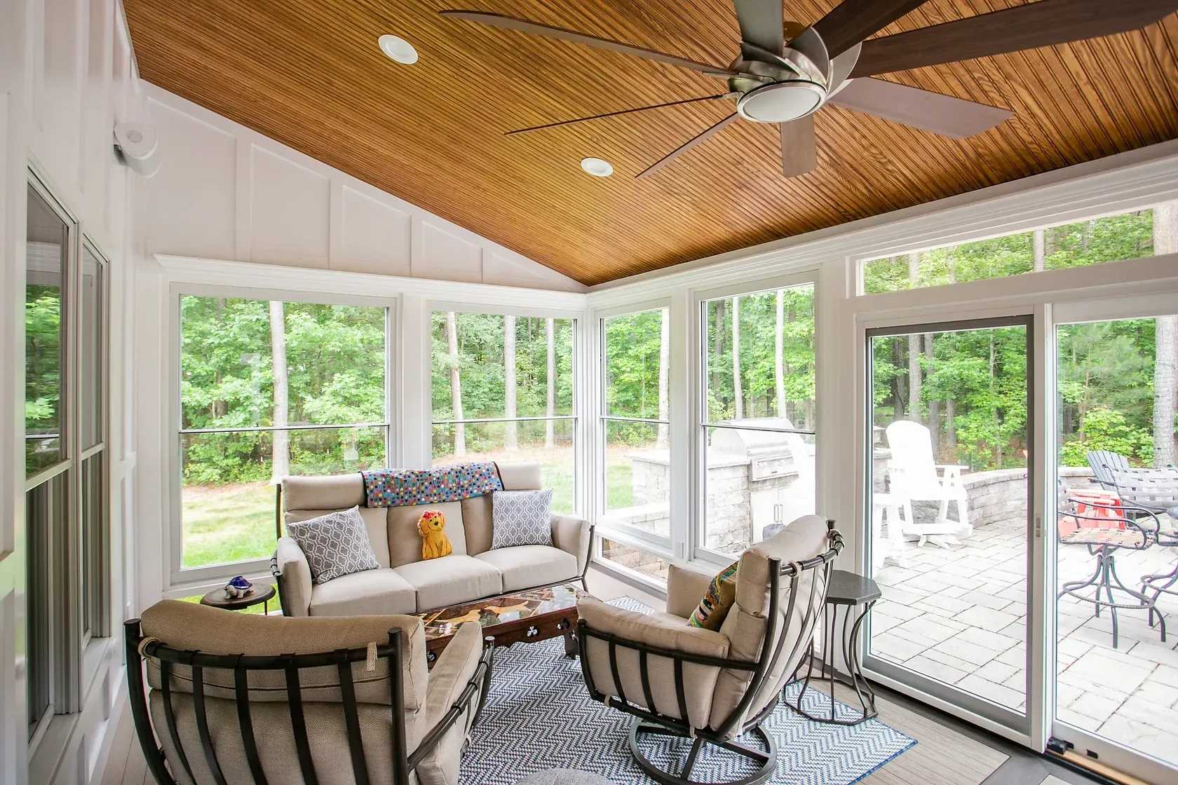 Sunroom with seating, large windows, ceiling fan, and wooden ceiling; overlooks a patio.