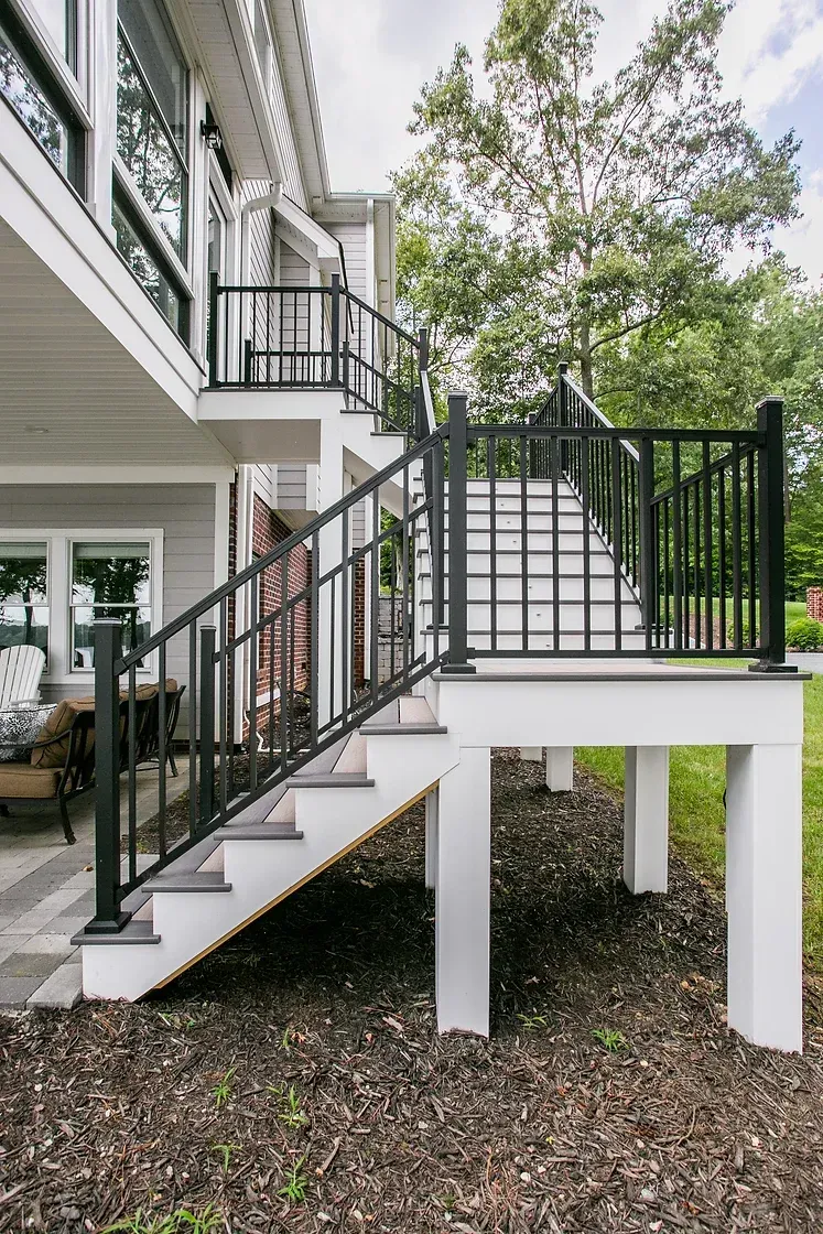 Exterior stairs with black railing and white supports leading up to a deck, against a house.