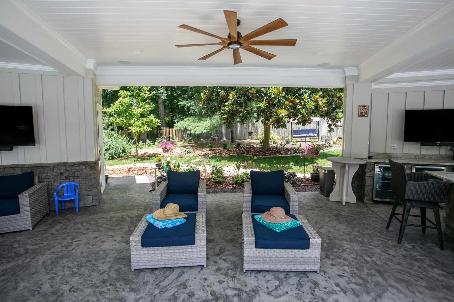 Covered patio with loungers, bar, and TVs overlooking a garden.