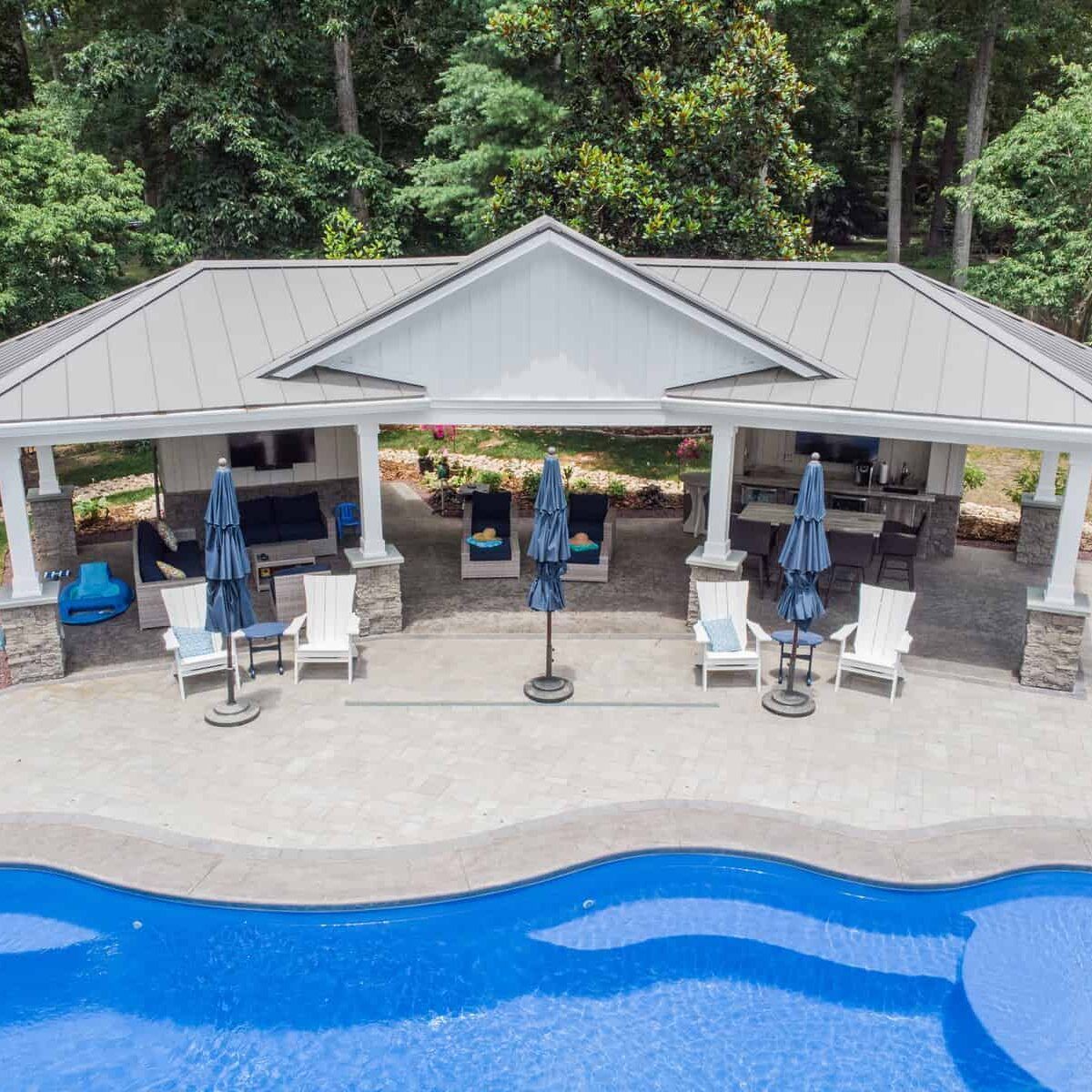 Outdoor poolside pavilion with seating, bar, umbrellas, and blue water.