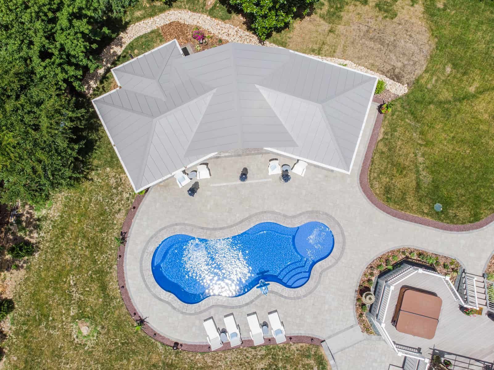 Aerial view of a house with a pool and patio; gray roof, blue water, and green grass.