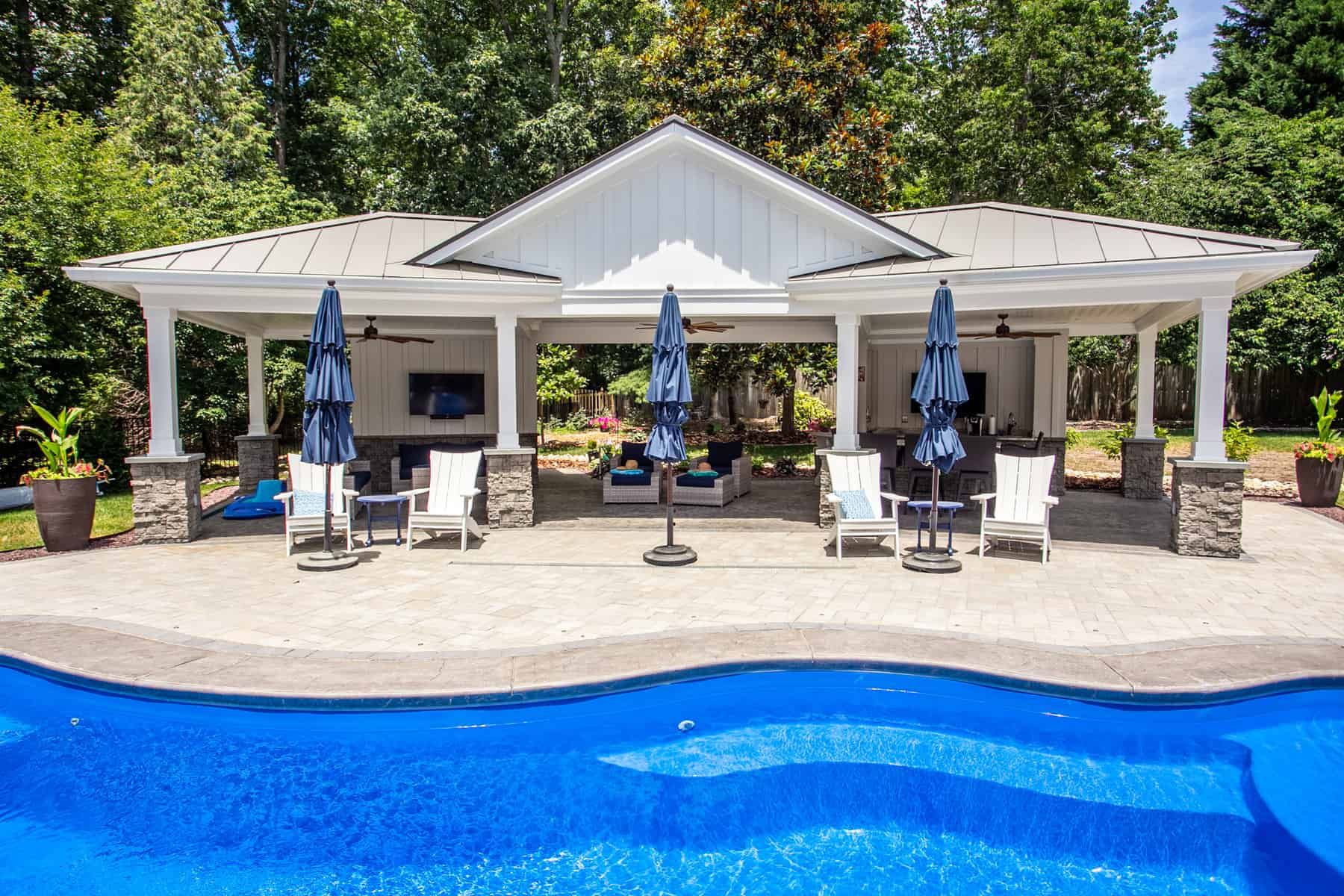 Poolside pavilion with blue umbrellas, outdoor seating, and a TV.