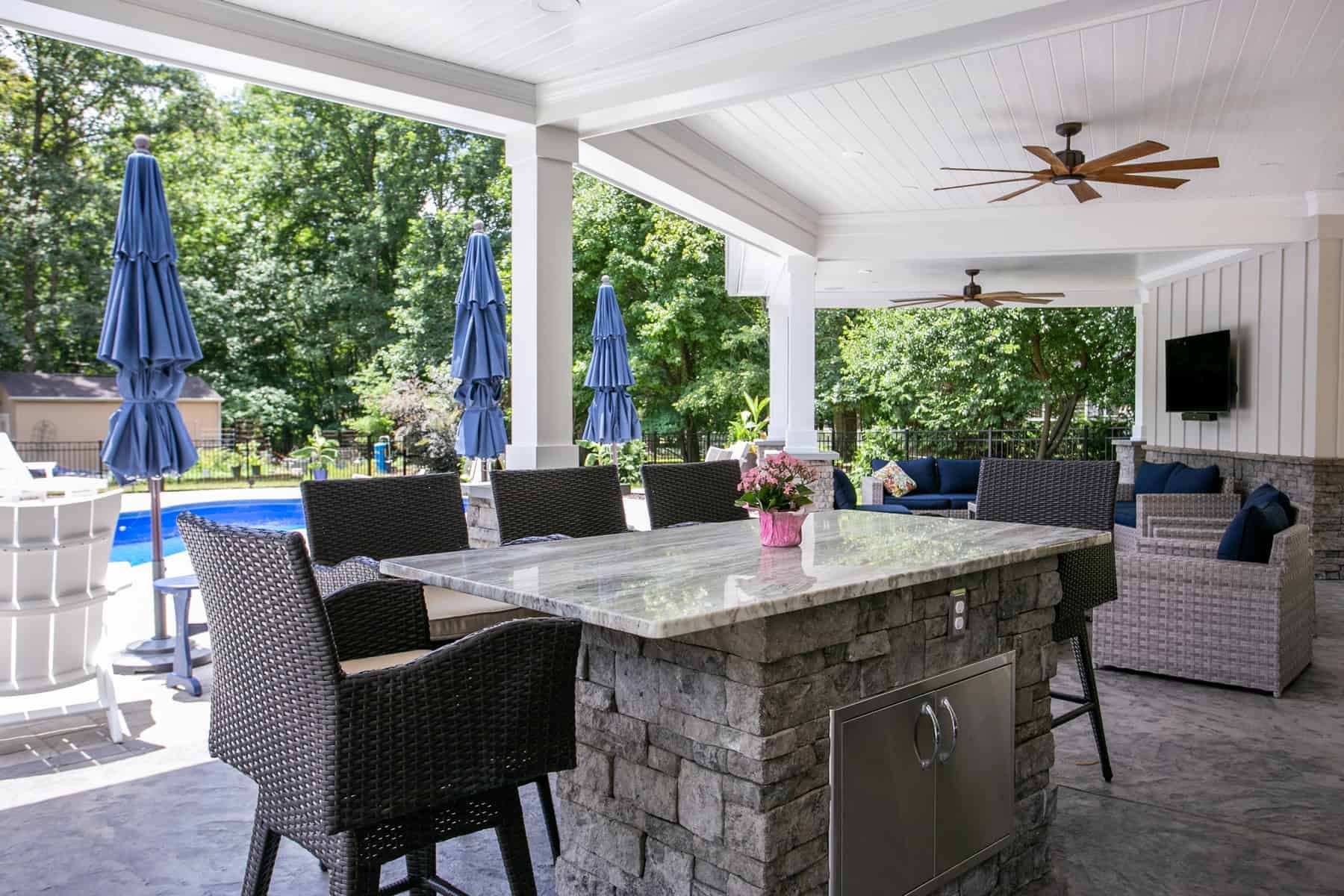 Covered patio with a stone island and seating overlooking a pool.