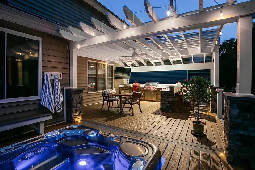 Outdoor deck with hot tub and covered seating area, evening lighting.