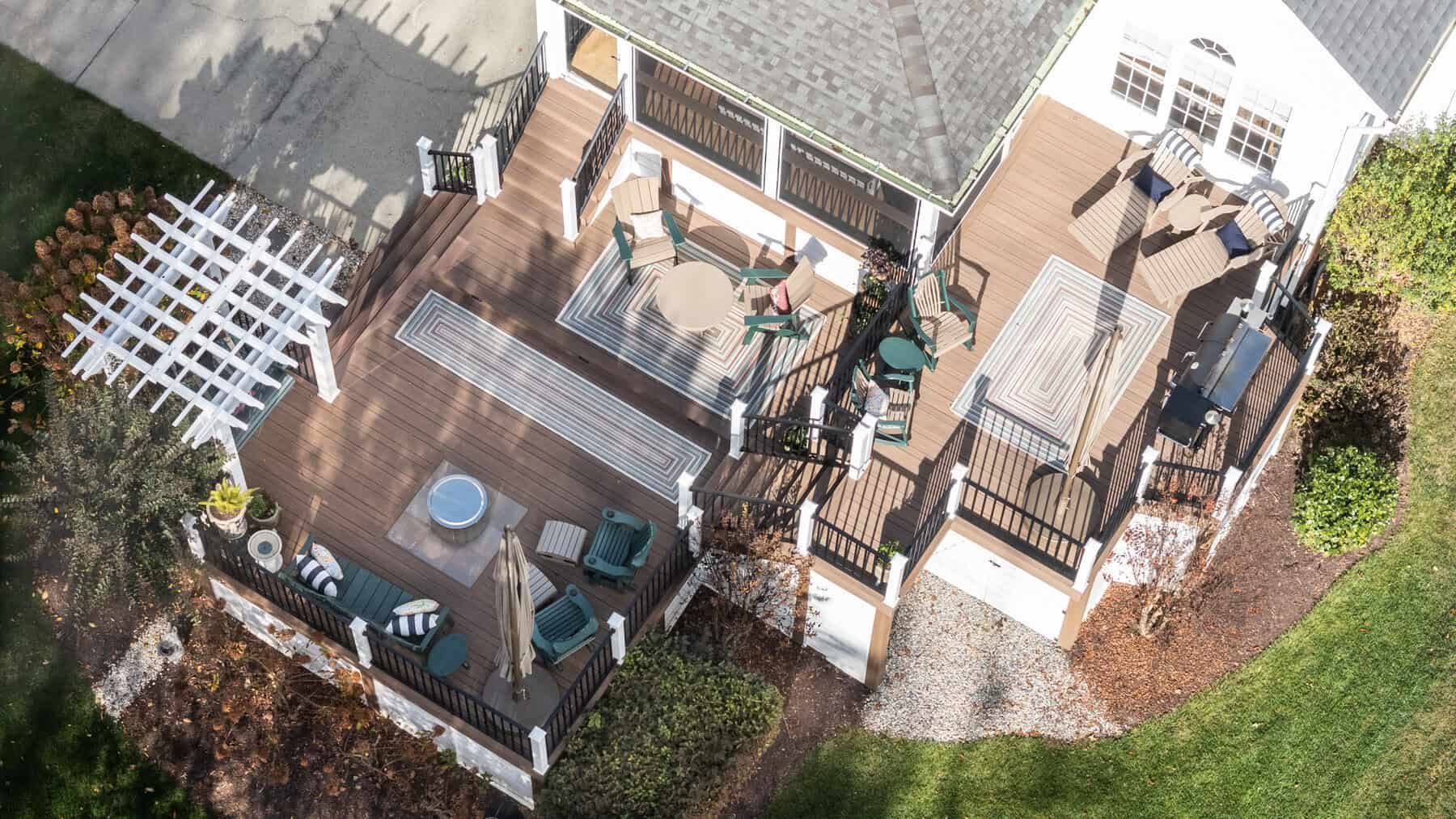Aerial view of a multi-level wooden deck with seating areas, a pergola, and a house in a yard.