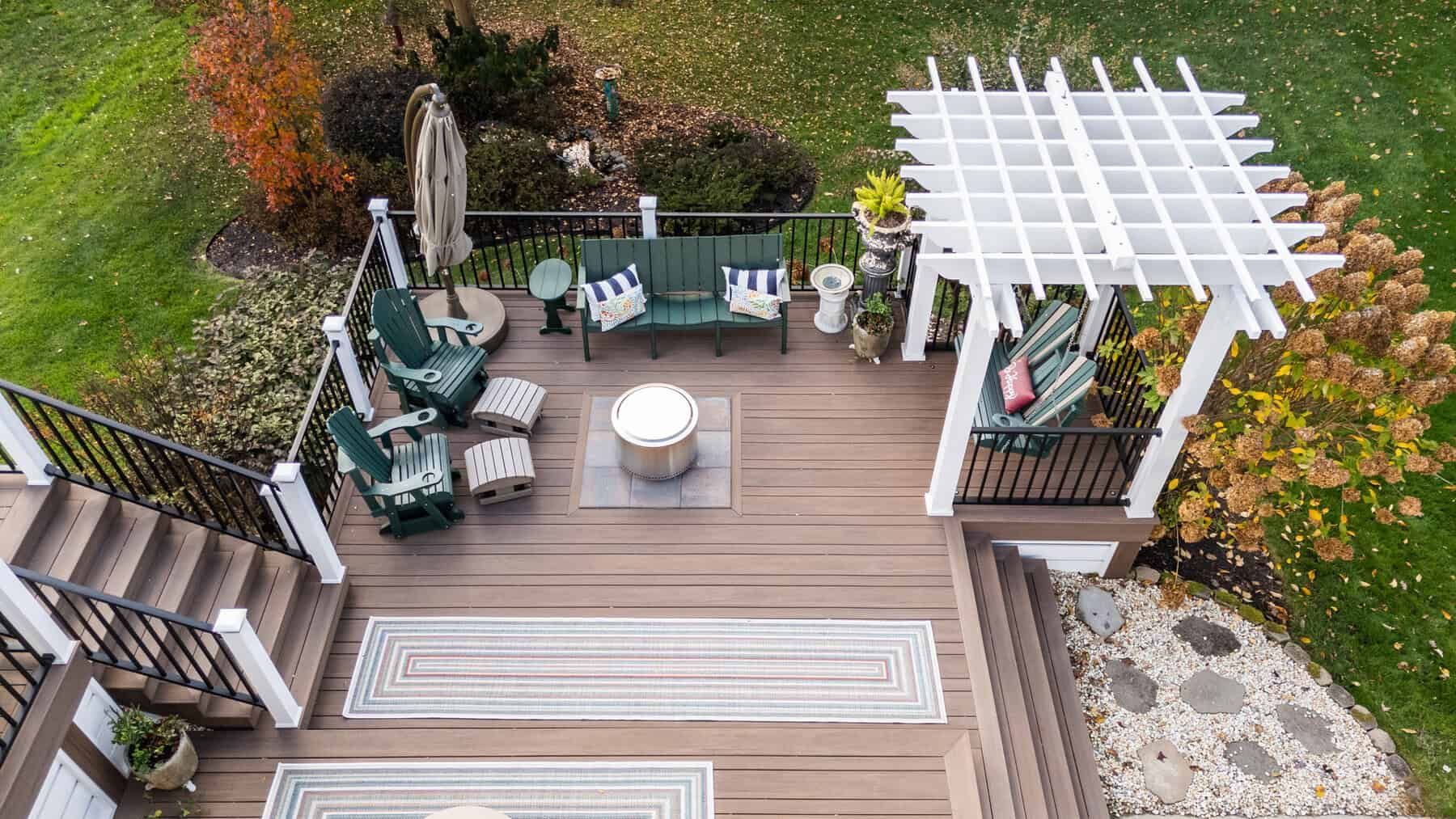 Aerial view of a wooden deck with seating areas, including a swing, benches, and a fire pit, surrounded by a lawn.