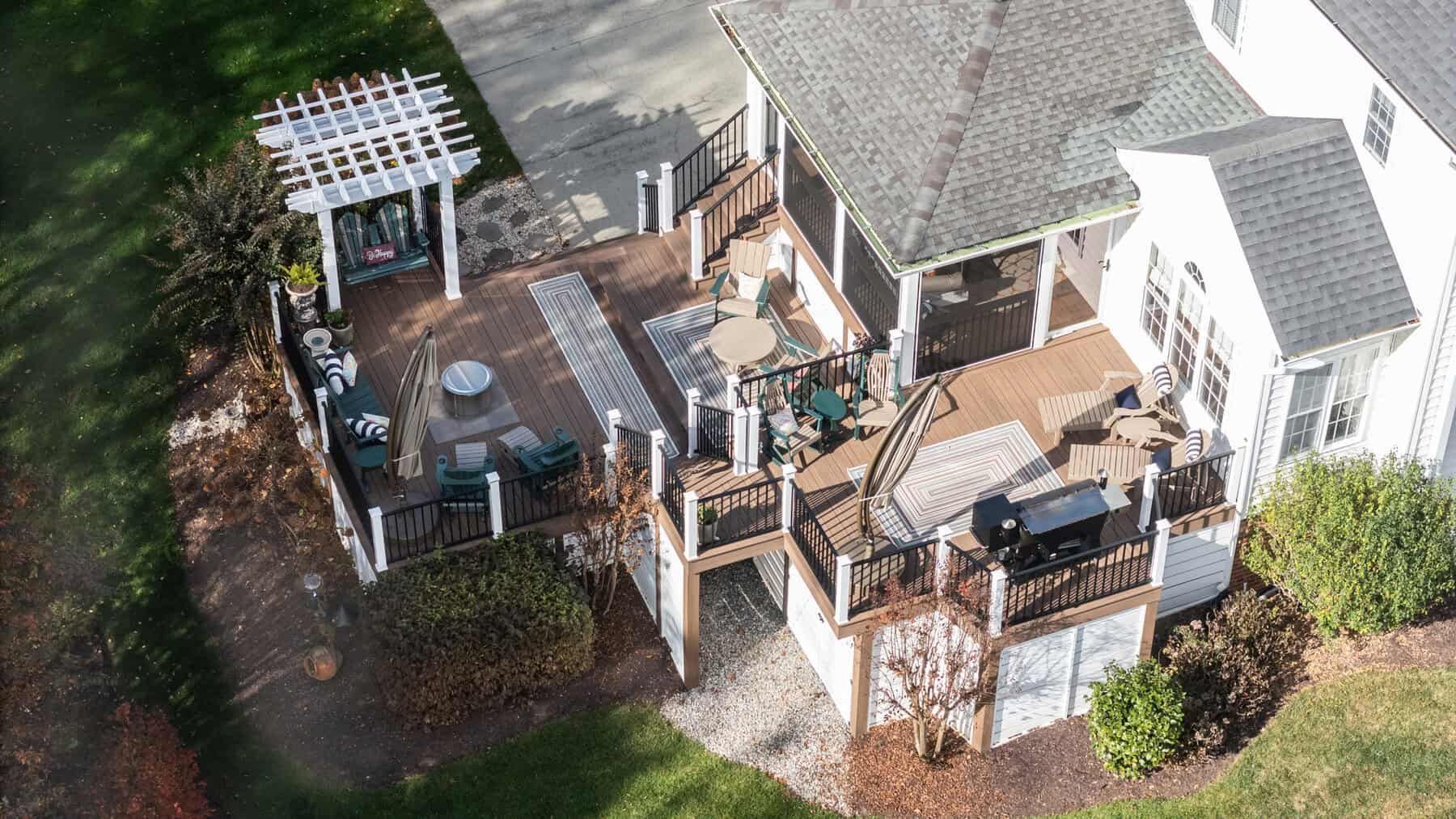 Multi-level wooden deck with pergola, screened porch, and grilling area connected to a white house with a grey roof.