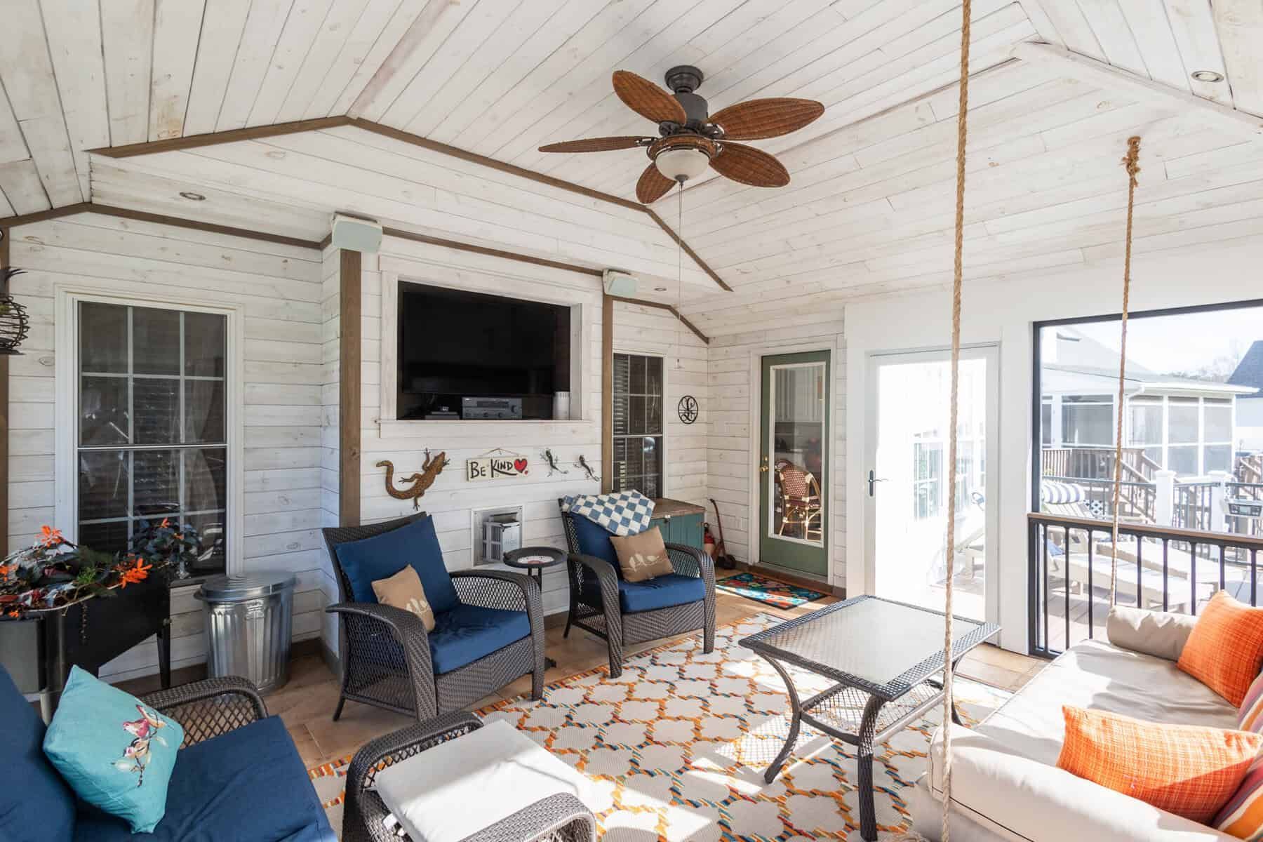 Sunroom with blue wicker furniture, rug, TV, and ceiling fan, with a swing and view of the outside.