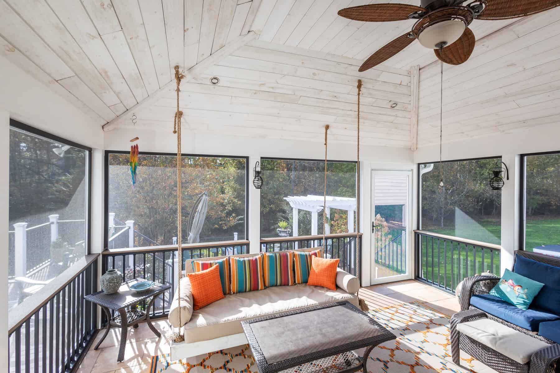 Screened porch with swing, white ceiling, black railings, and colorful cushions.