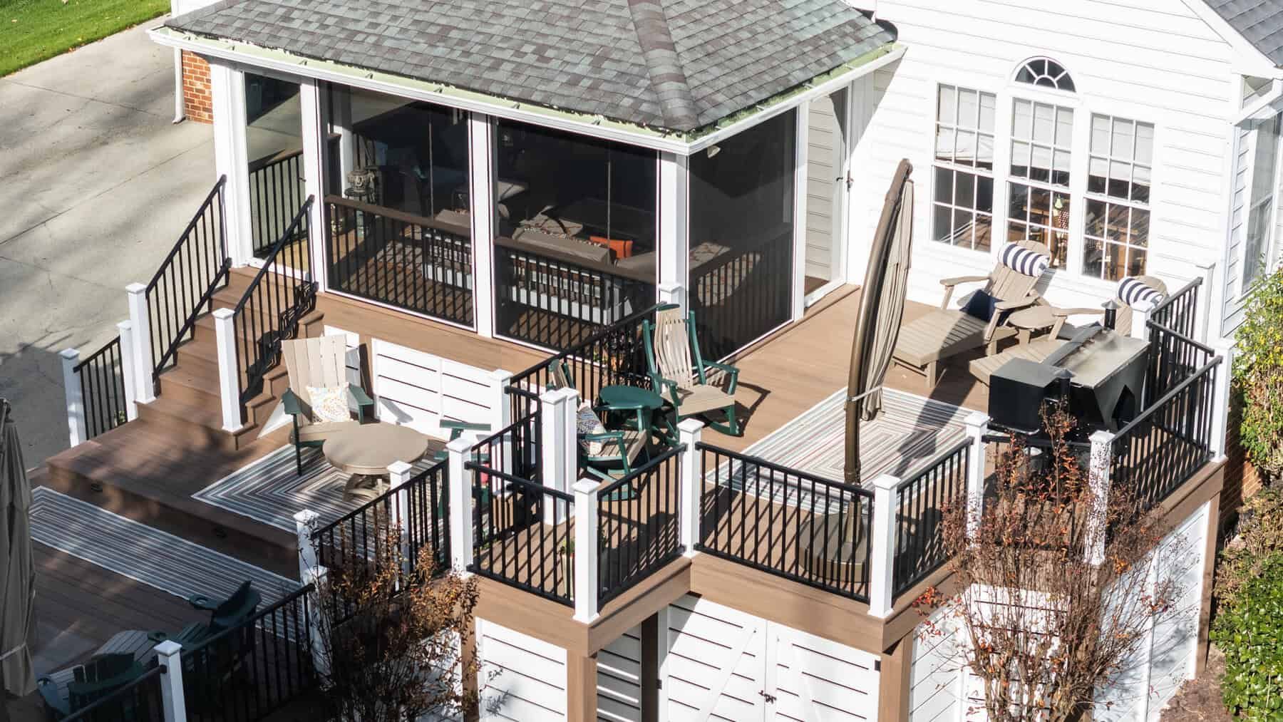 Multi-level deck attached to a white house, with screened porch and outdoor furniture. Brown and white tones.