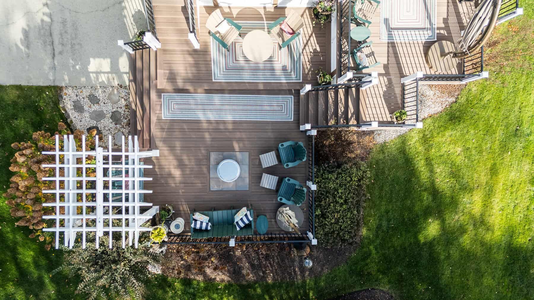Overhead view of a wooden deck with outdoor furniture, surrounded by greenery and a white trellis.