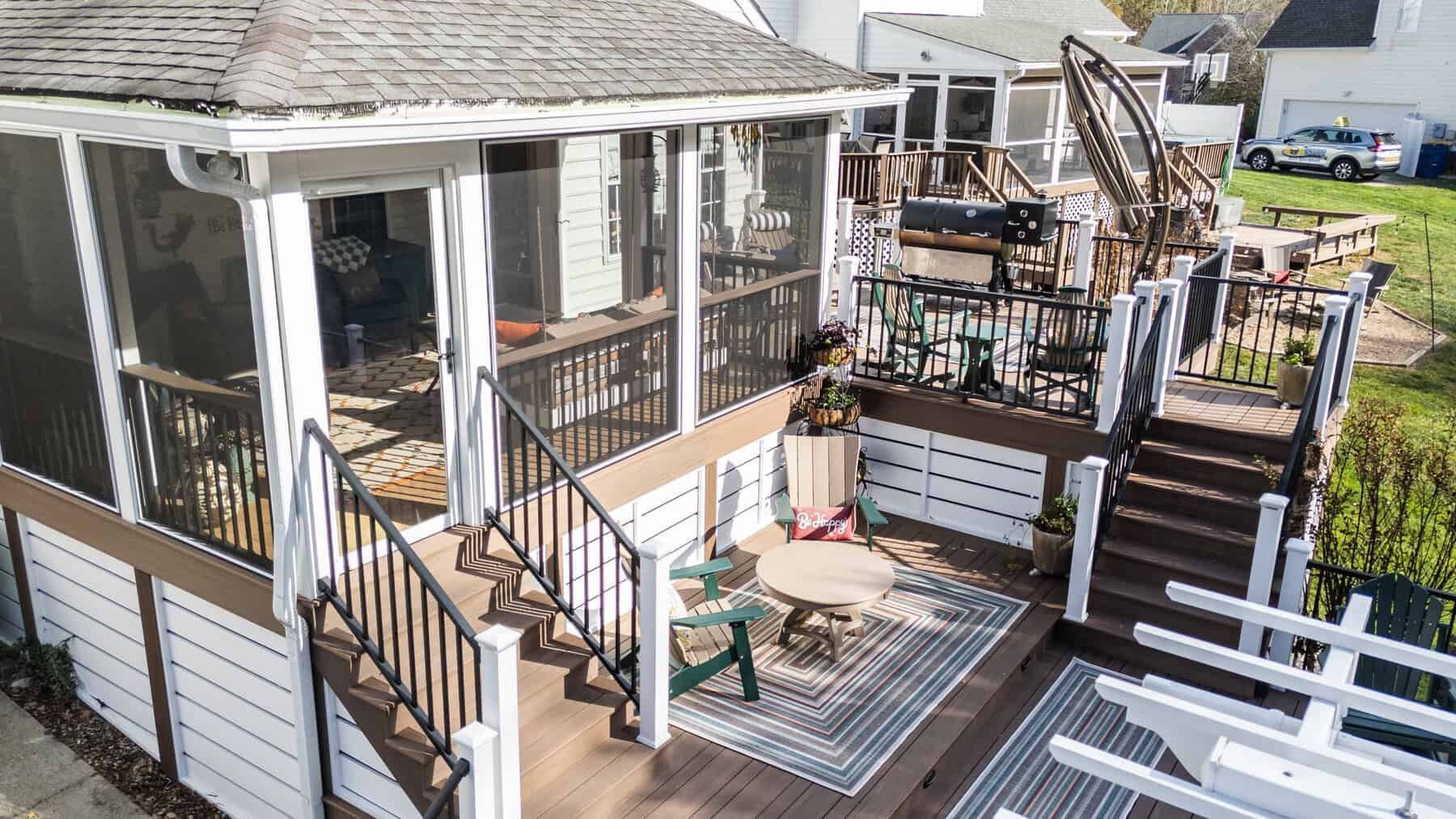 Screened-in porch and deck with stairs, surrounded by white siding and railings, brown decking.