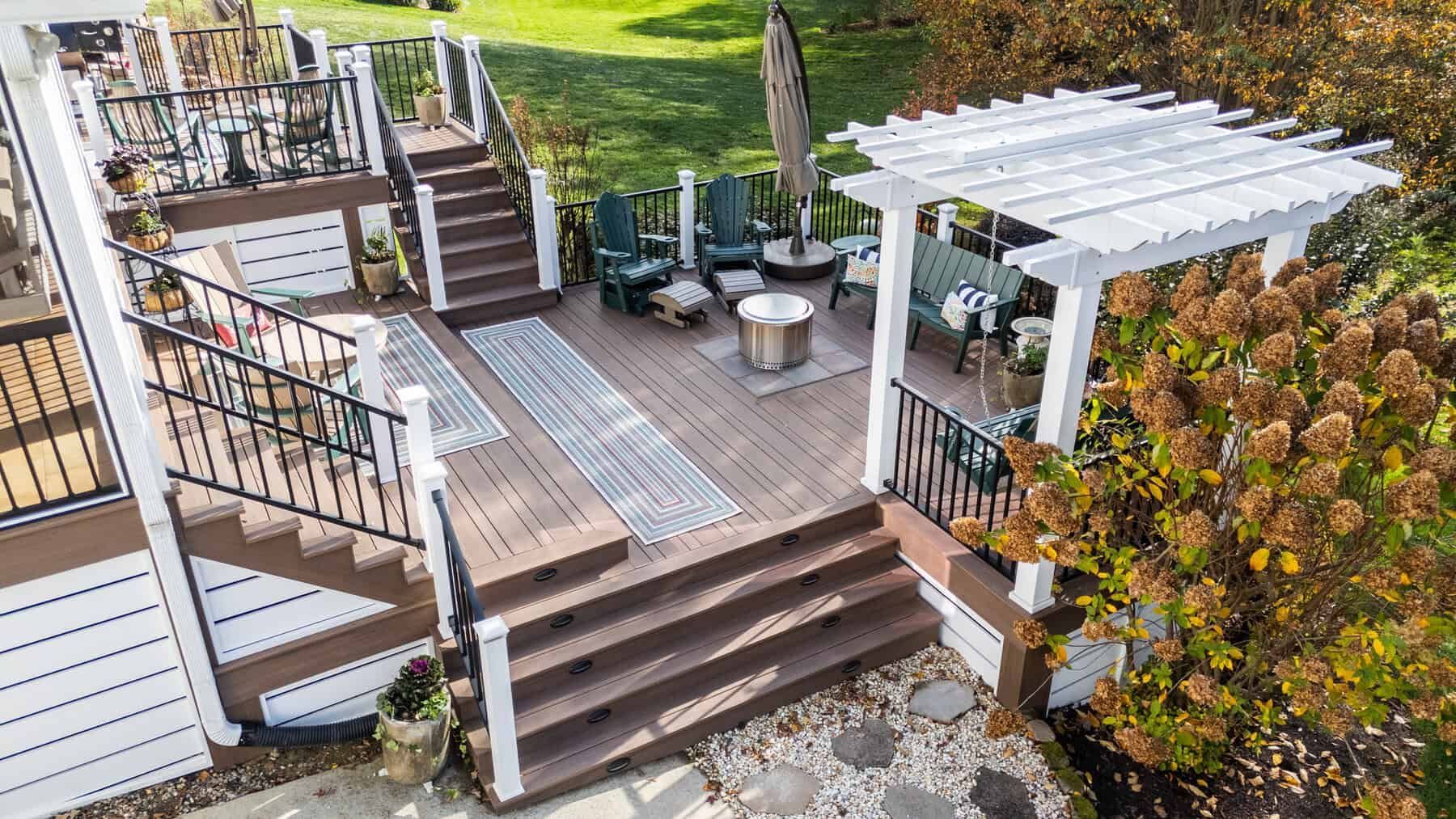 Multi-level deck with steps, a pergola, and outdoor seating. Brown and white with a lawn in the background.