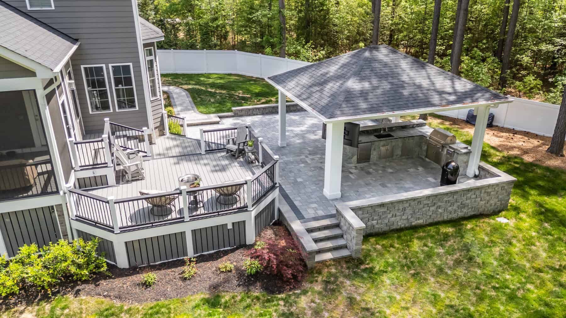 Backyard patio with deck, stone patio with gazebo, and lush green lawn.