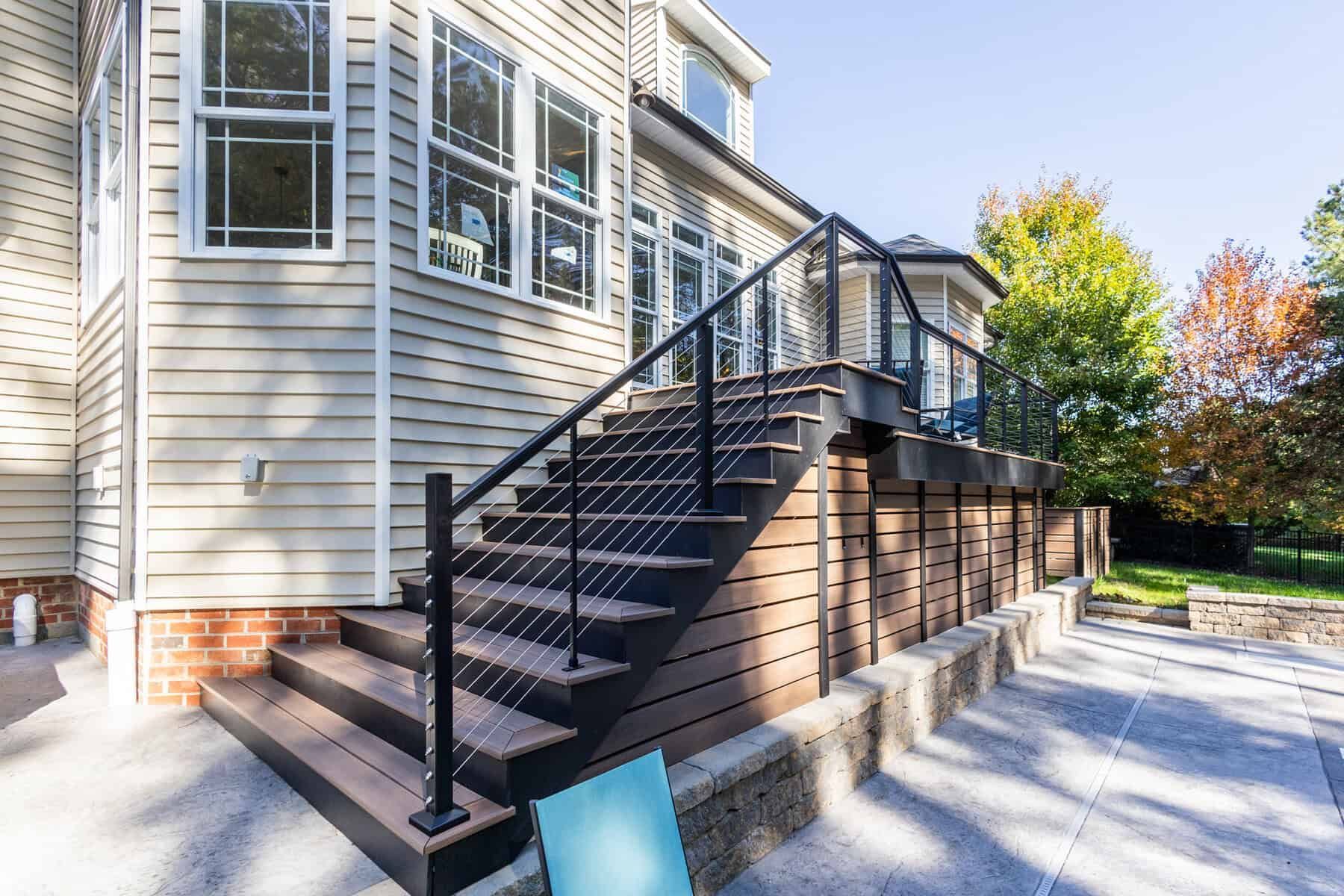 Wooden deck with stairs, black railing, and gray siding on a house.