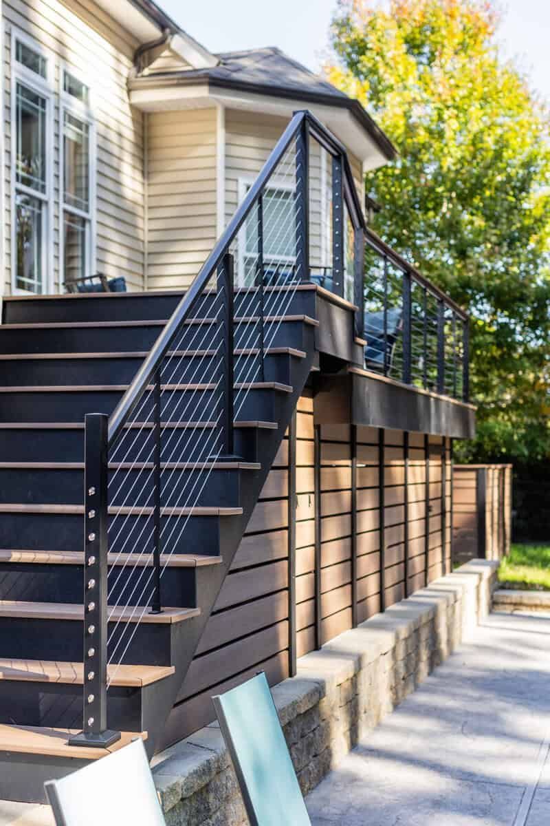 Exterior view of a deck with dark steps and black railing, adjacent to a light-colored house.
