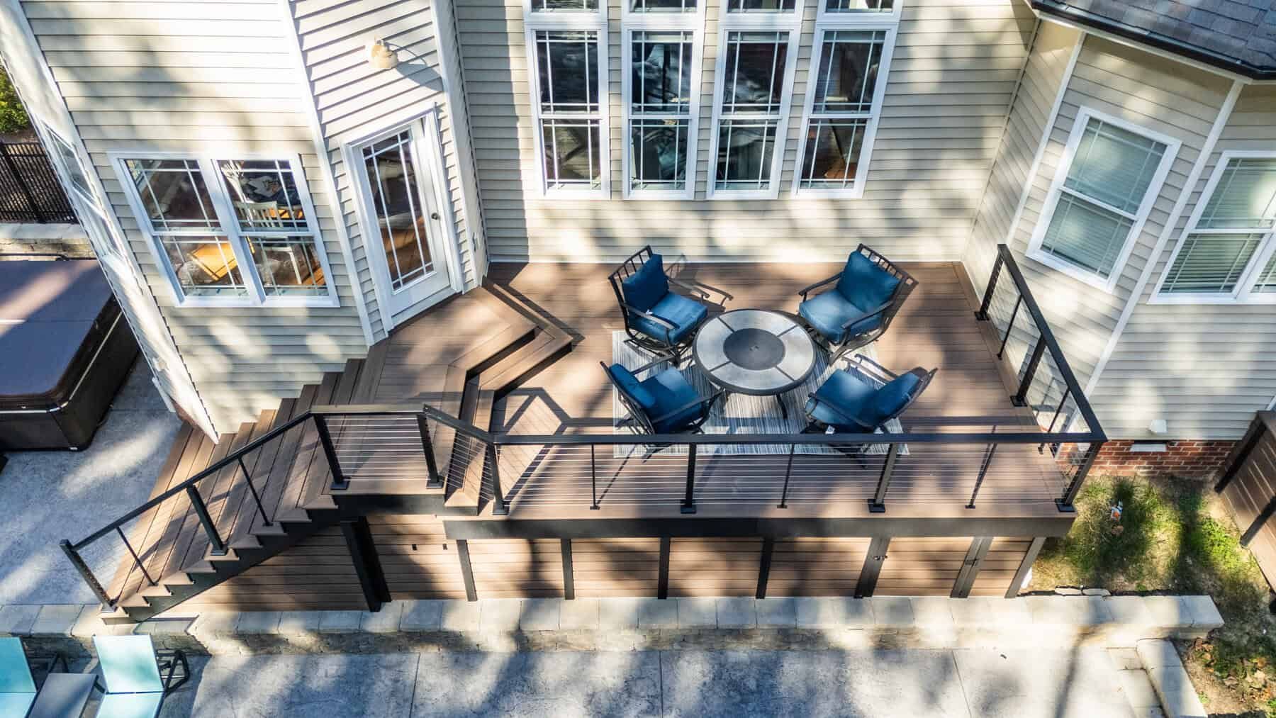 Overhead view of a deck with seating, fire pit, and stairs connected to a light-colored house.