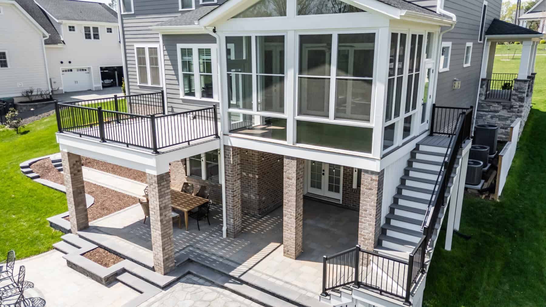Two-story home with a screened porch and deck. Stairs and a dark railing are visible. The house has gray siding.