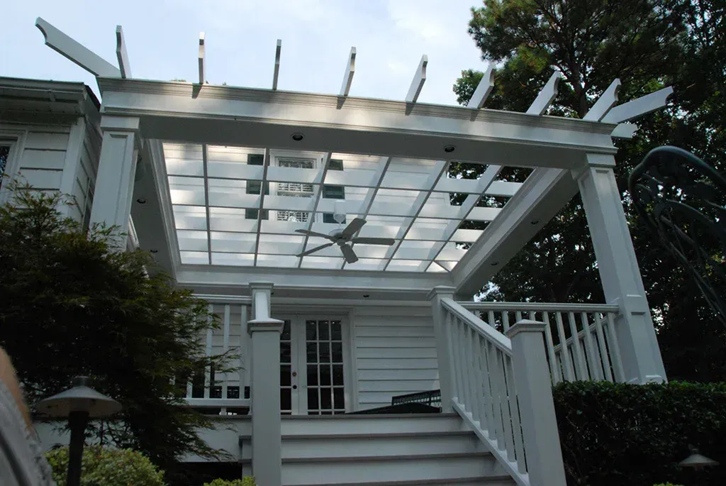 White pergola over a deck with stairs, a ceiling fan, and glass panels.