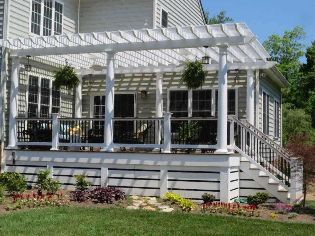 White pergola over a raised deck with steps, a black railing, and potted plants.