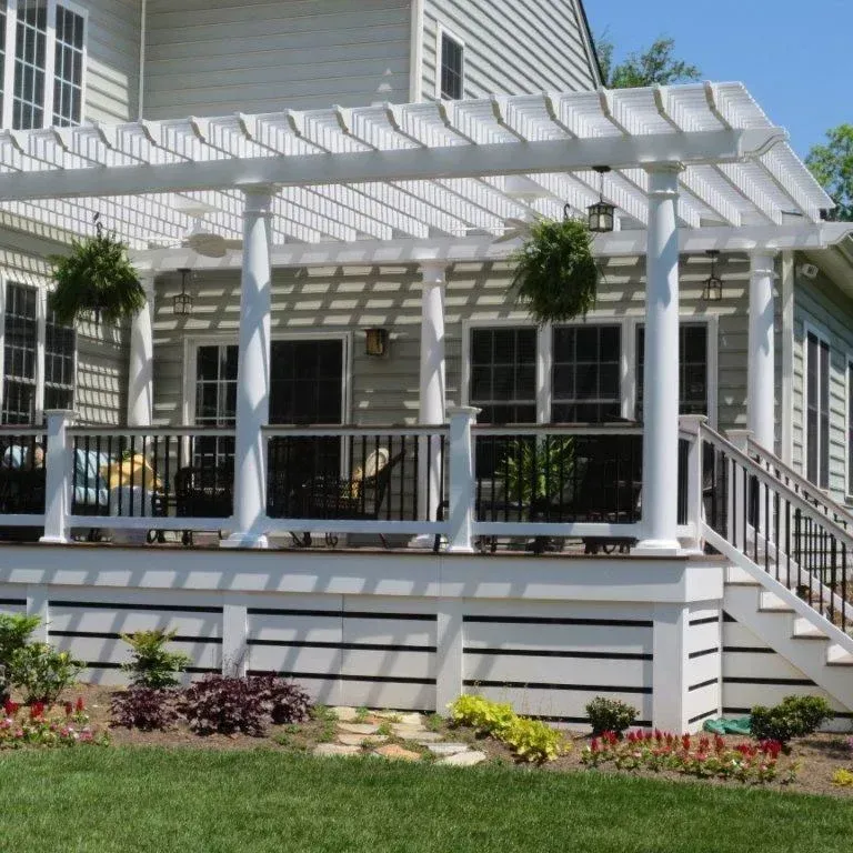 White pergola over a deck with hanging plants, stairs, and a house in the background.