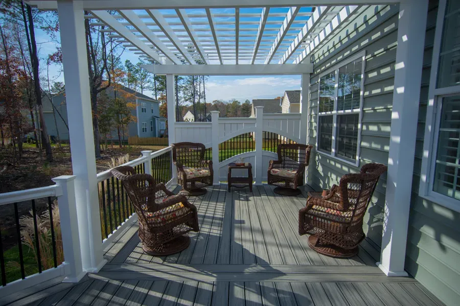 Covered porch with wicker chairs, pergola, and view of houses.