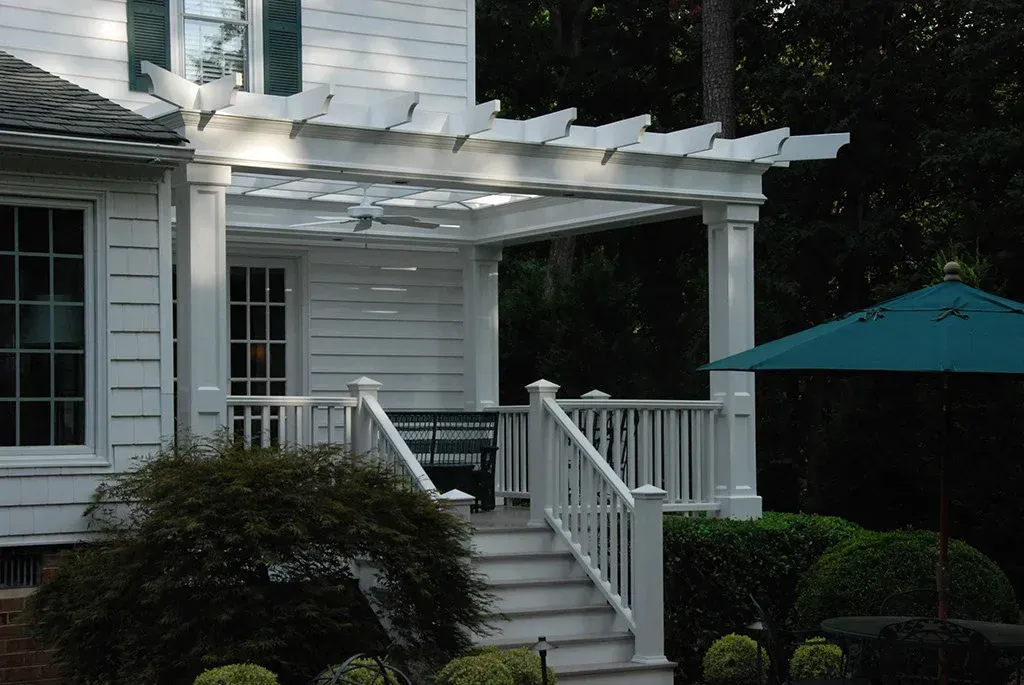 White porch with pergola, steps, and railing. A teal umbrella is visible.