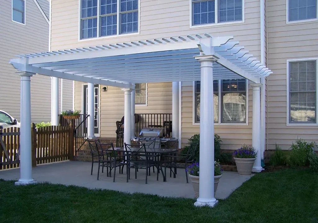 White pergola over a patio with a dining set, near a house with windows.