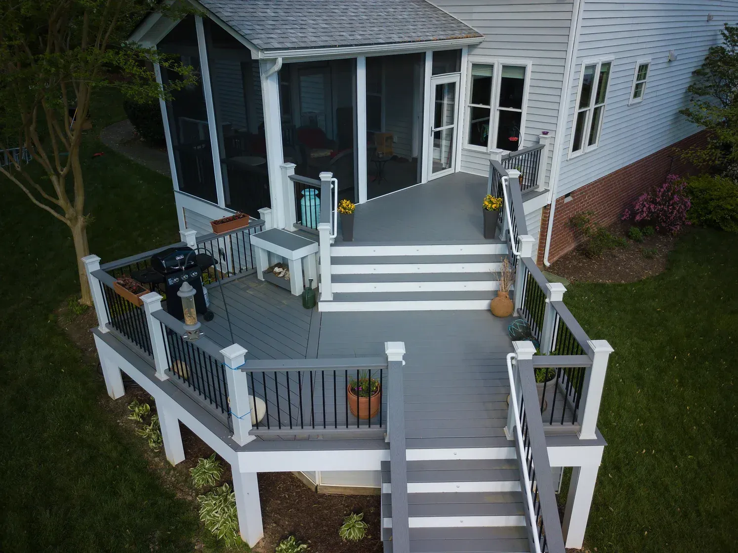 Overhead view of a multi-level gray deck attached to a white house with a screened porch and green lawn.